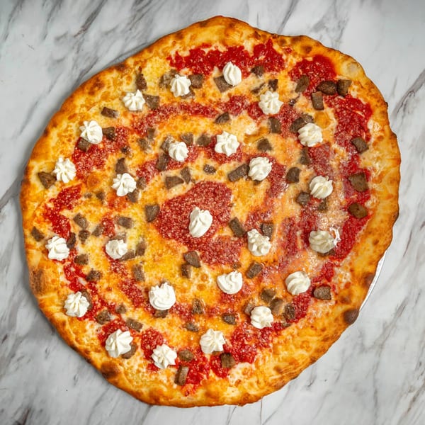 Round pizza with red sauce, cheese, sausage, and dollops of ricotta on a marble surface.