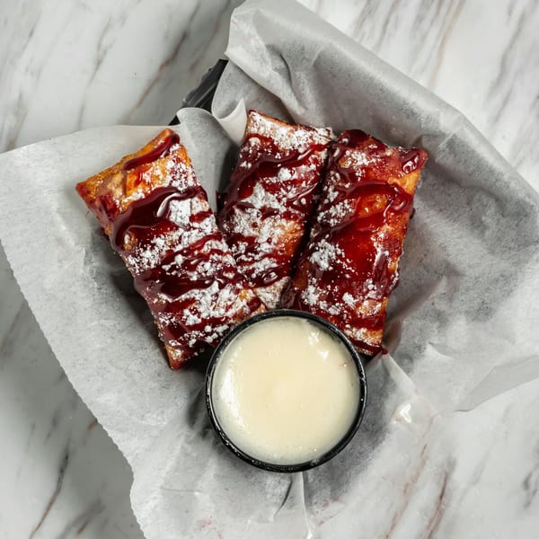 Three fried pastries drizzled with red sauce and powdered sugar, with a side of white dipping sauce.