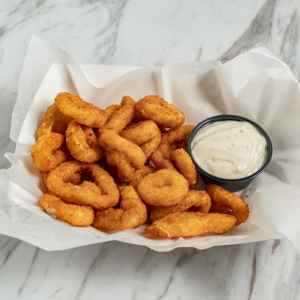 A basket of golden-brown onion rings with a side of creamy white dipping sauce.